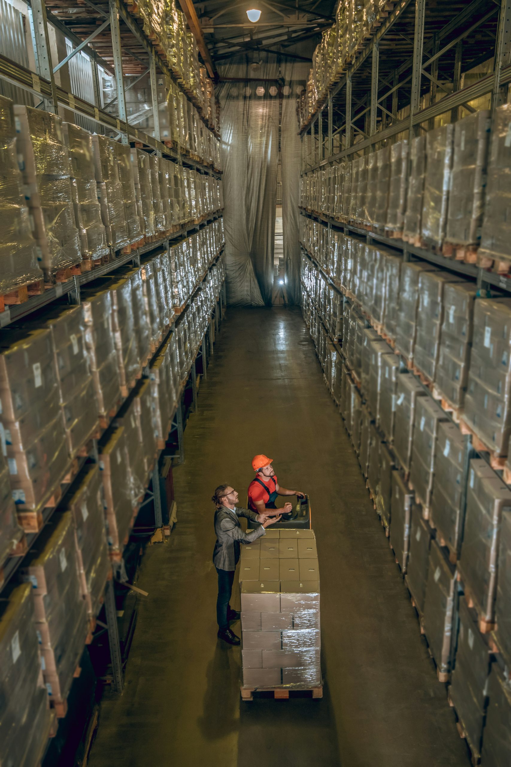 Warehouse staff review palletized inventory in a high-density storage aisle—illustrating the visibility, space utilization, and replenishment challenges that Nvexus helps mid-market companies manage more efficiently.